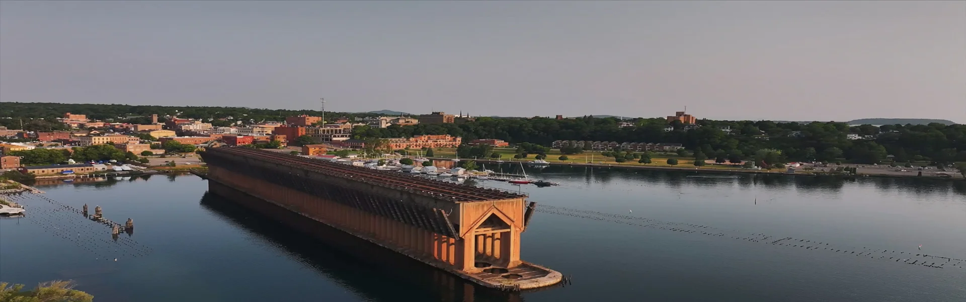 Aerial view of the Lower Harbor Ore Dock in Marquette, Michigan, surrounded by calm water and with a backdrop of the town and greenery.