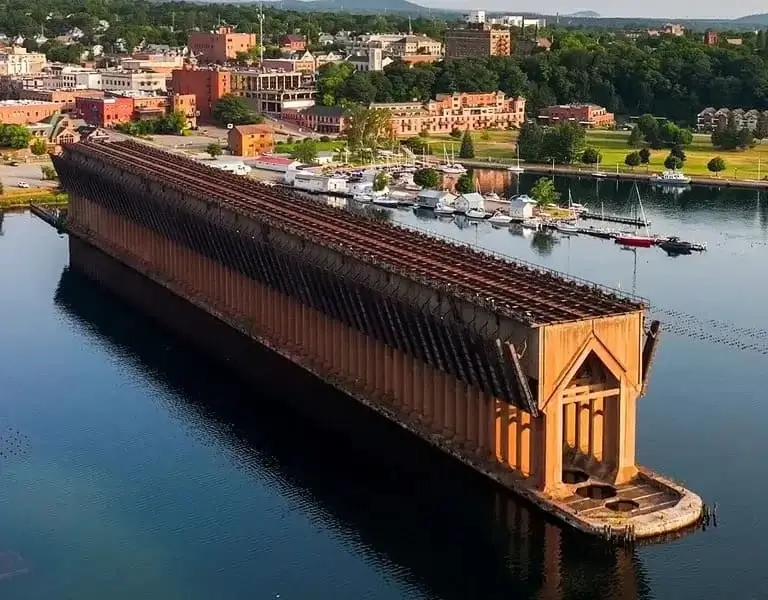 Aerial view of the Lower Harbor Ore Dock in Marquette, Michigan, surrounded by calm water and with a backdrop of the town and greenery.